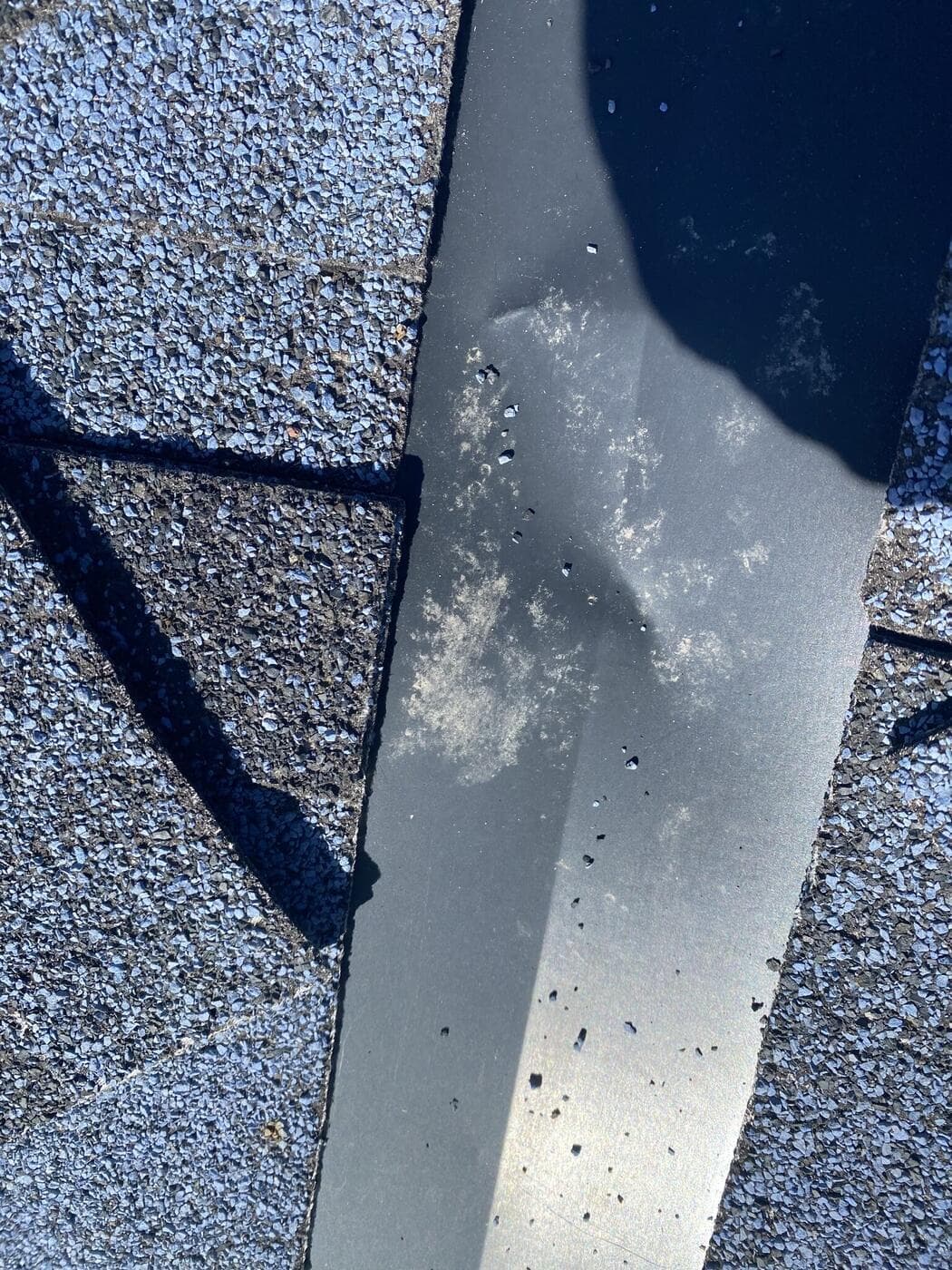 Hail impact marks pitting the metal valley flashing on a Calgary roof