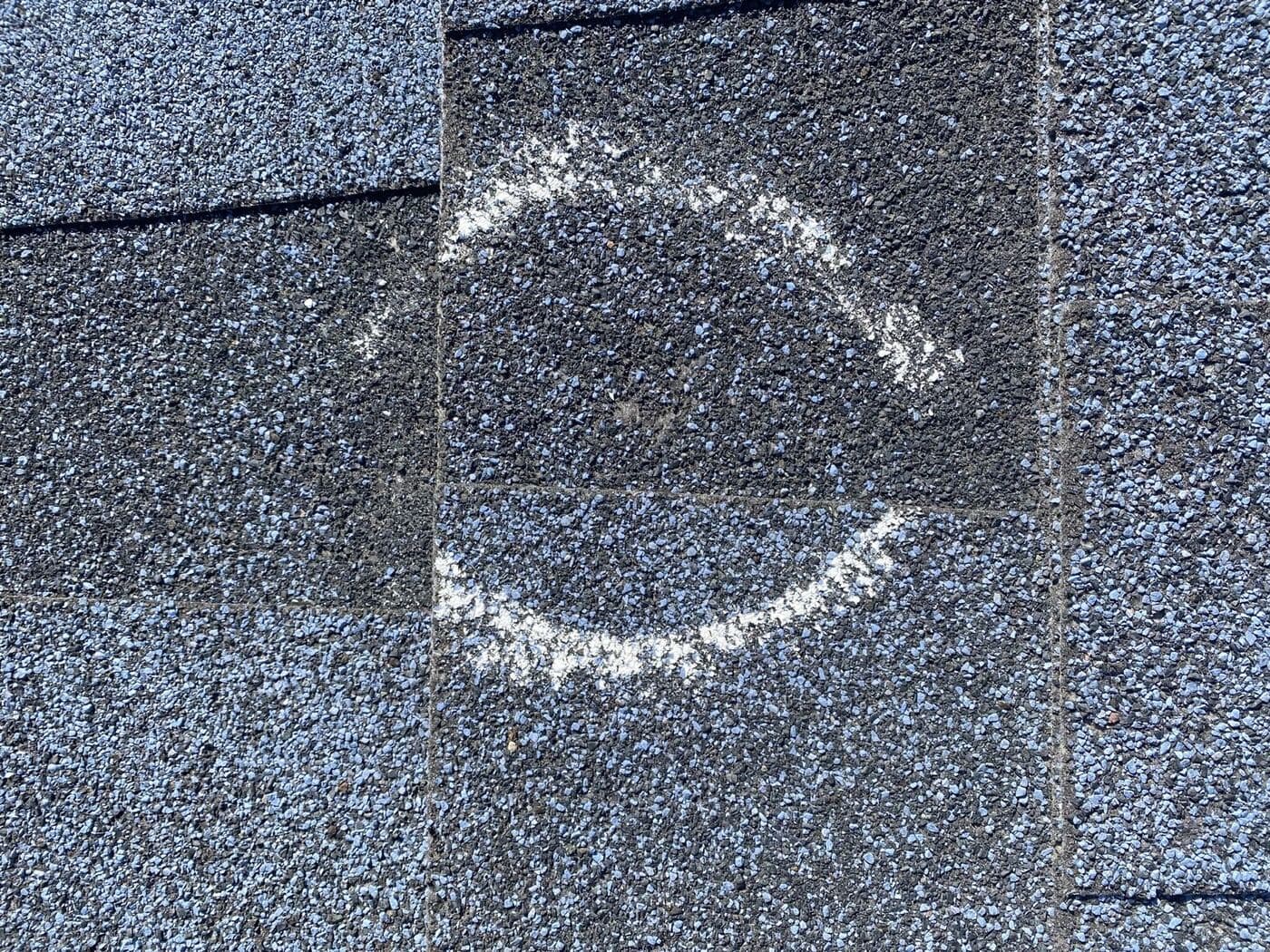 Chalked test square on an asphalt shingle roof with a hail impact circled inside it