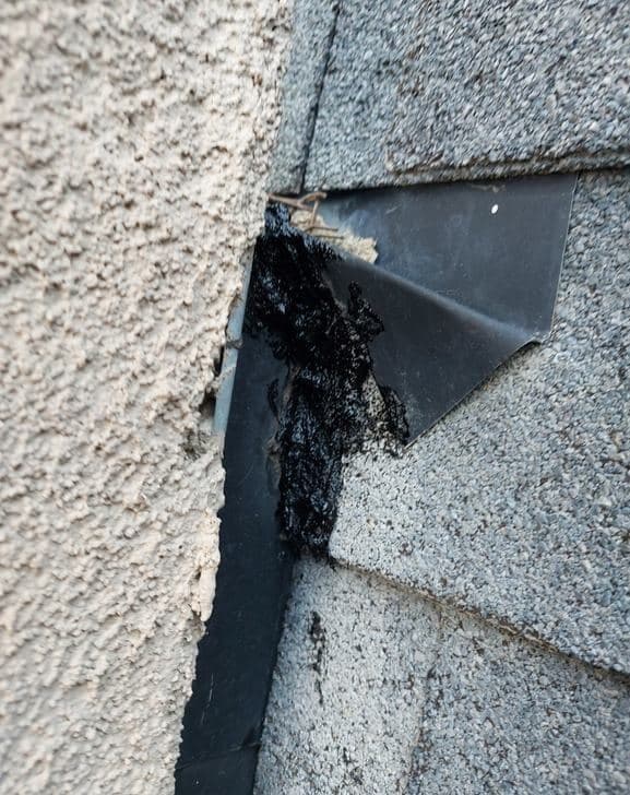 Black mastic troweled over a stucco wall and roof transition as a previous repair