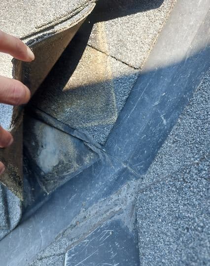 Shingle lifted at a valley to show the detail underneath during a roof inspection
